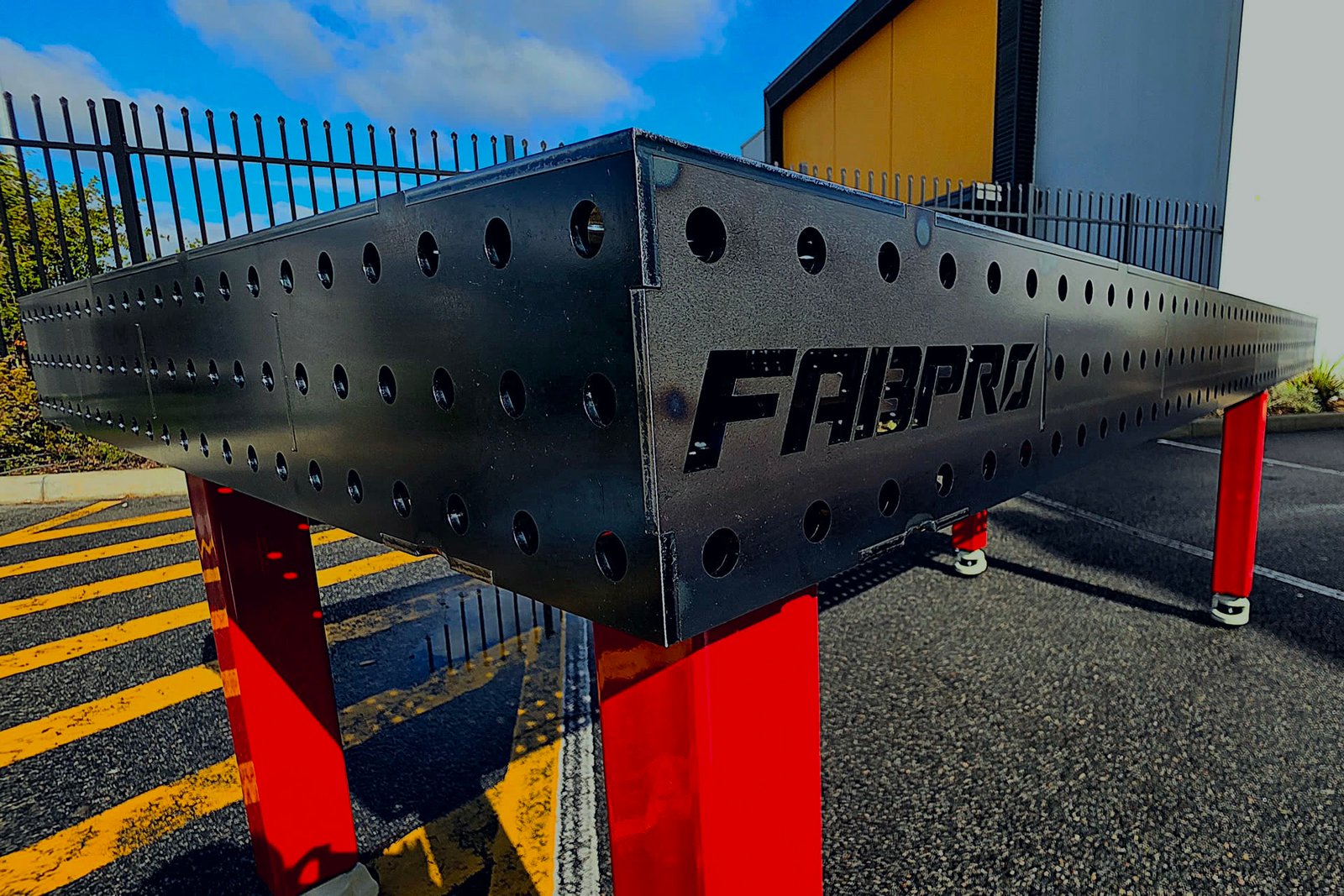 FabPro welding table, black steel top with a 16mm hole grid and red legs